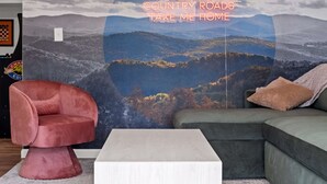 A room with a large landscape painting, a red chair, a green sofa, and a white coffee table. - Rolling Hills/Hot Tub/Firepit/Mins to ACE+NRG (Oak Hill)