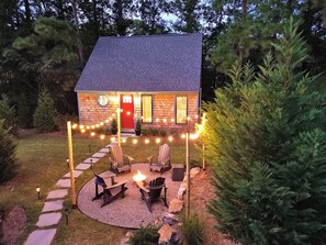 Uma casa pequena com porta vermelha, lareira e área de estar externa.