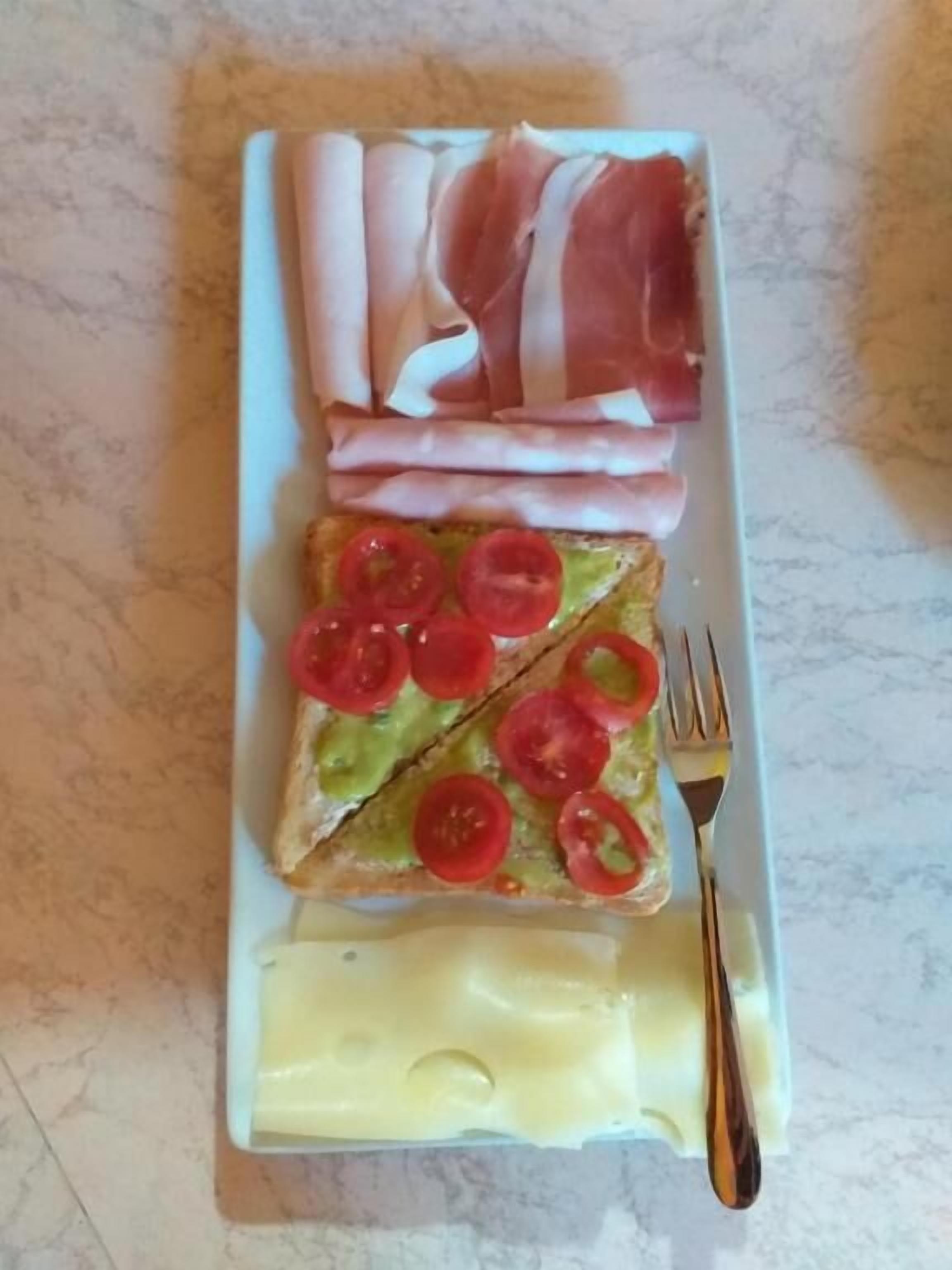 Une assiette avec des tranches de pain garnies de tranches de tomates, d’une tranche de fromage et de plusieurs tranches de jambon.