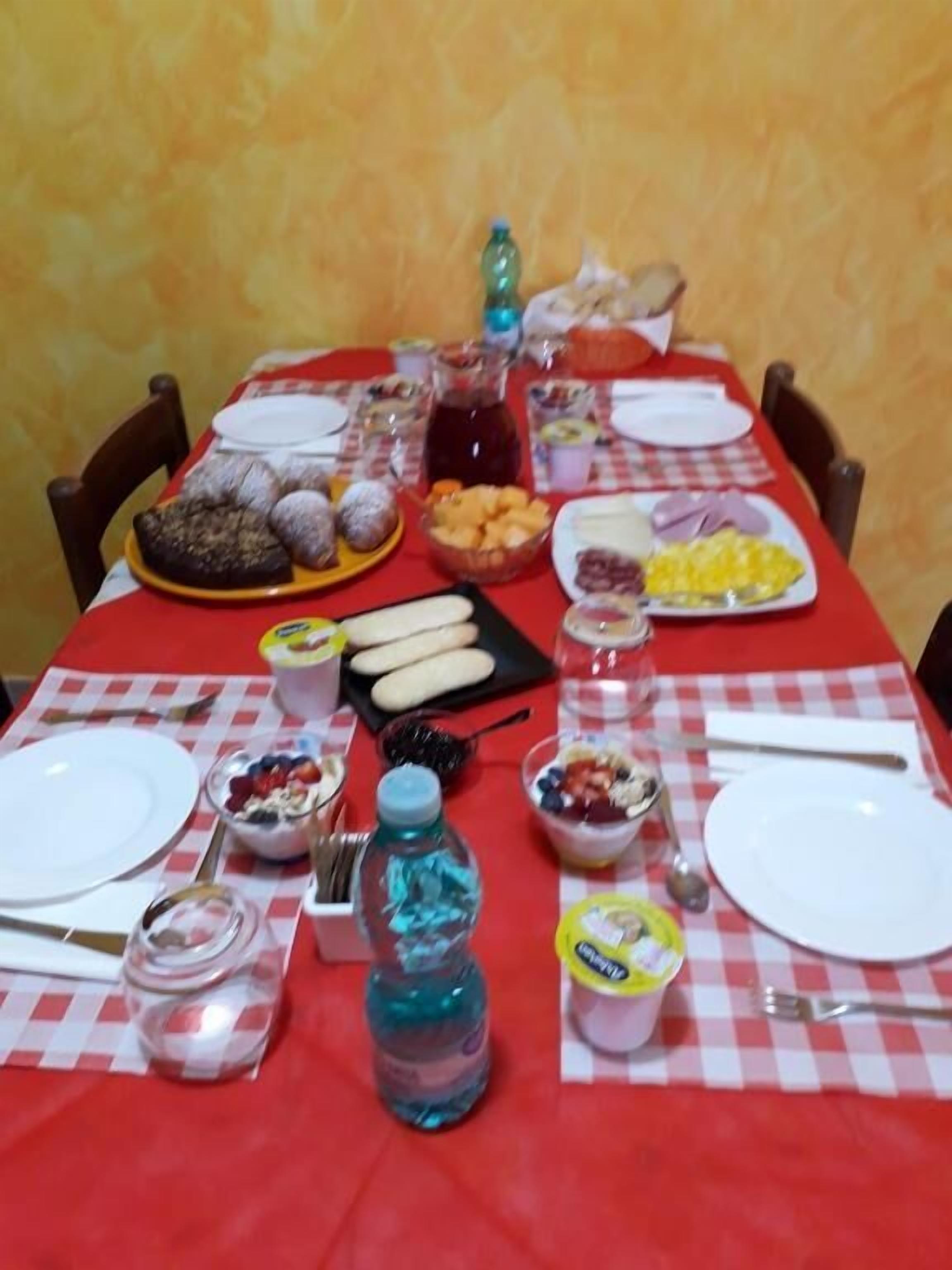Una mesa de comedor servida con varios platos, entre ellos pan, frutas y una botella de agua.