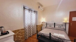 A bedroom with a bed, bedside lamps, a nightstand, a window with patterned curtains, and a door. - AFFITTACAMERE IL GIRASOLE (Sant'Anna Arresi)