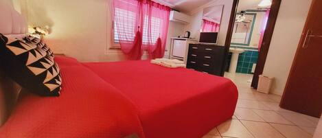 A hotel room with a red bed, a small desk, a mirror, and a bathroom visible through an open door.