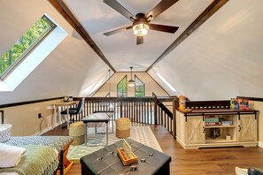 A cozy loft bedroom with a skylight, a ceiling fan, a small dining area, and a wooden cabinet with storage.