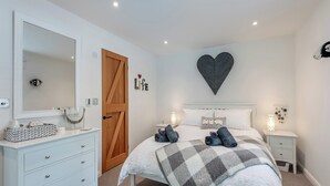 Une chambre à coucher comprenant un lit, des tables de chevet, une commode, un miroir, une porte en bois et un élément décoratif mural en forme de cœur.