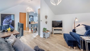 Un salon moderne comprenant un téléviseur, un canapé et un coin repas avec une table et des chaises en bois.