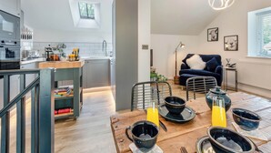 Une cuisine moderne avec un coin repas, comprenant une table en bois dressée pour le petit-déjeuner, un canapé bleu et des luminaires suspendus.