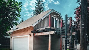 Una casa de dos pisos con un garaje, una pequeña terraza al aire libre y una escalera que lleva a un balcón.