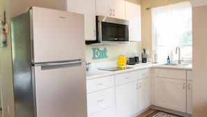Una cocina con armarios blancos, un refrigerador de acero inoxidable, un microondas y un lavamanos.