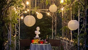 An outdoor garden setting with a gazebo, string lights, and a table with a cake and candles.
