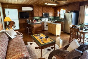 A cozy cabin-style kitchen with wooden cabinets, a central island, and a dining area with a table and chairs. - Private, cabin with endless Hill Country views. Horse & dog friendly! (Pipe Creek)