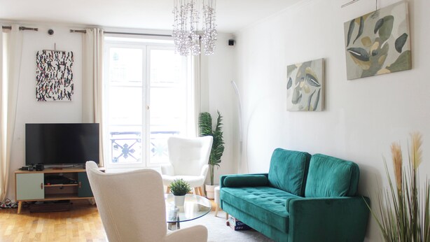 A modern living room with a television, a white chair, a teal sofa, and abstract wall art.