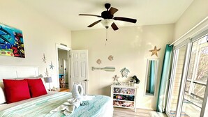 Une chambre à coucher comprenant un lit, un ventilateur de plafond, une commode, une coiffeuse et une grande fenêtre.