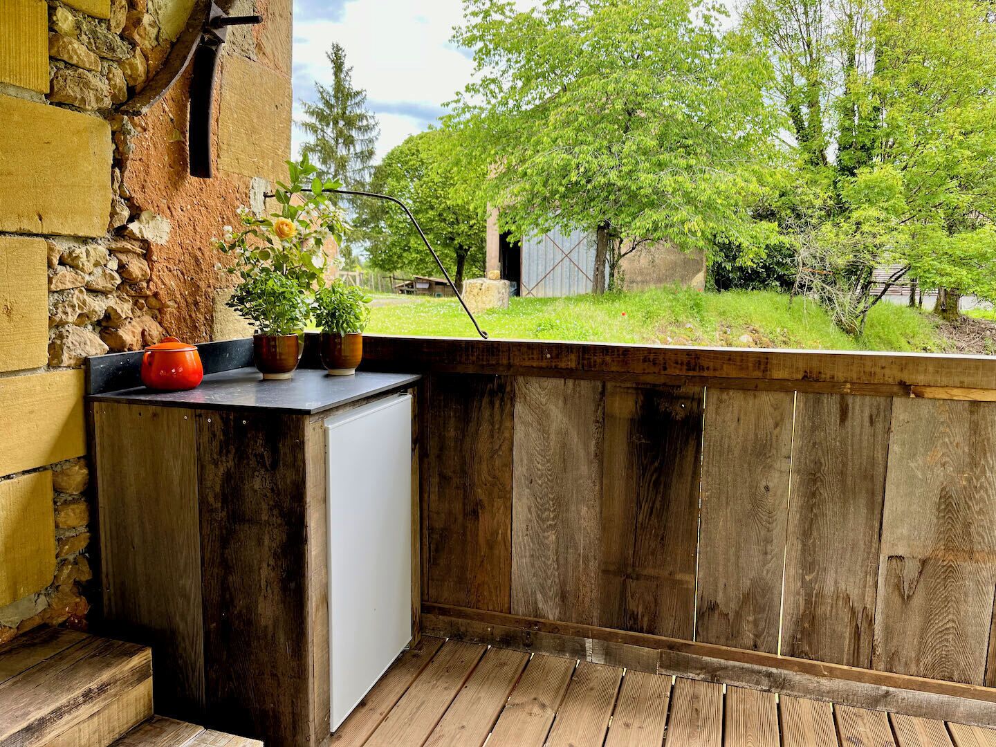 Un balcon en bois rustique, avec un mur en pierre, un petit réfrigérateur blanc et des plantes en pot.