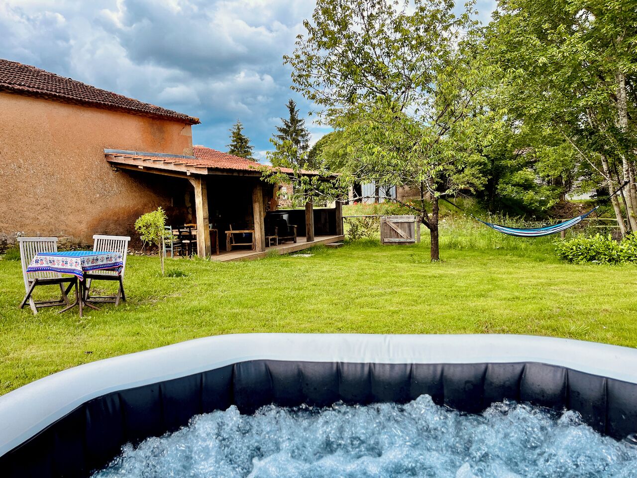Una vasca idromassaggio all'aperto con area verde, un pontile in legno e una zona salotto coperta.