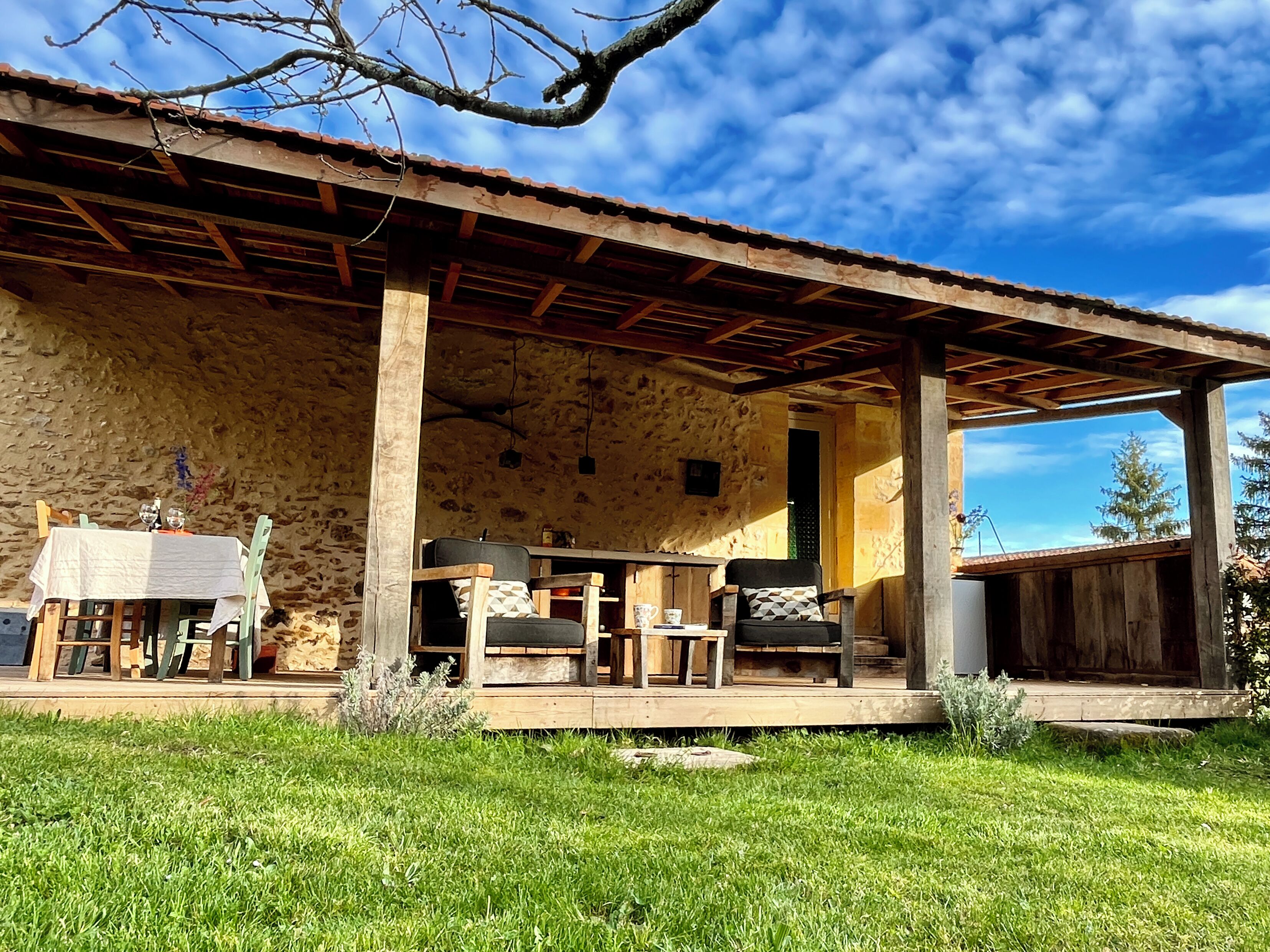 A rustic stone building with a covered patio area featuring wooden furniture and a table.
