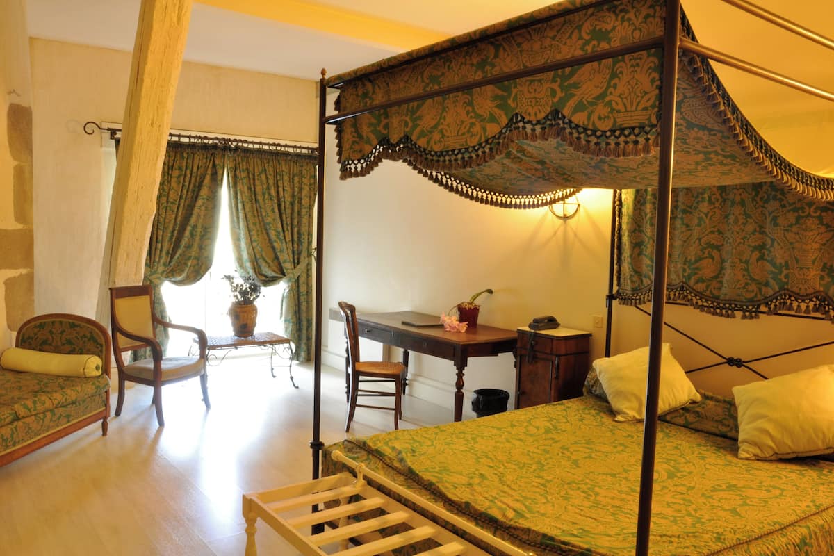A four-poster bed with a canopy, a desk with a chair, a sofa, and a potted plant.