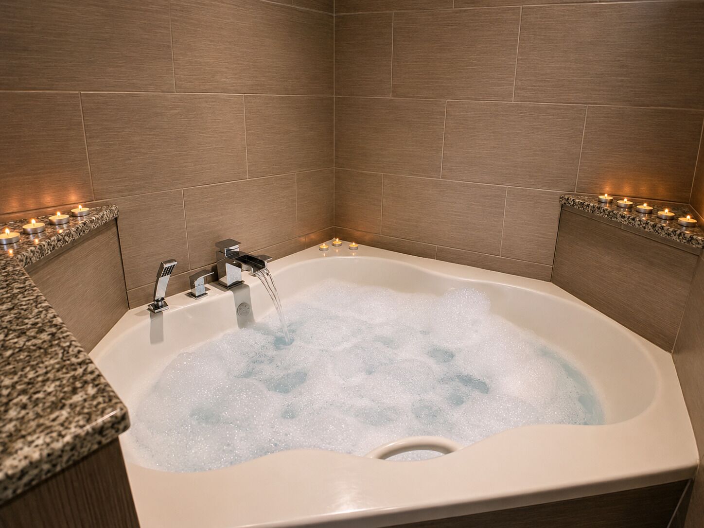 A bathroom with a bathtub filled with bubbles, a faucet, and candles on the sides.