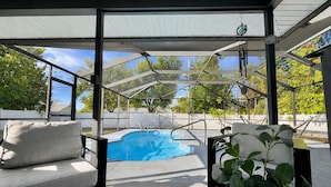 A covered outdoor area with a pool, a cushioned seating area, and a potted plant. - House w/ Pool, Hot Tub & Backyard (Cape Coral)