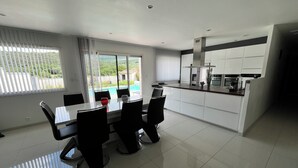 Een moderne keuken met witte kasten, een eethoek met een glazen tafel en uitzicht op een zwembad.