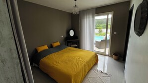 Een slaapkamer met een bed, een bureau, een stoel, een groot raam en uitzicht op een zwembad.