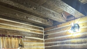 Ein Blockhauszimmer mit Bett, einem fenster mit Vorhängen und einer Hängelampe.