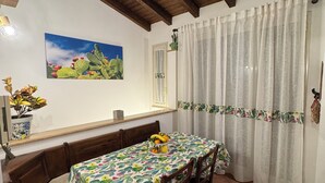 A dining area with a wooden bench, a table with a cactus-themed tablecloth, and a window with a view of a landscape. - The sweet little house (Palermo)