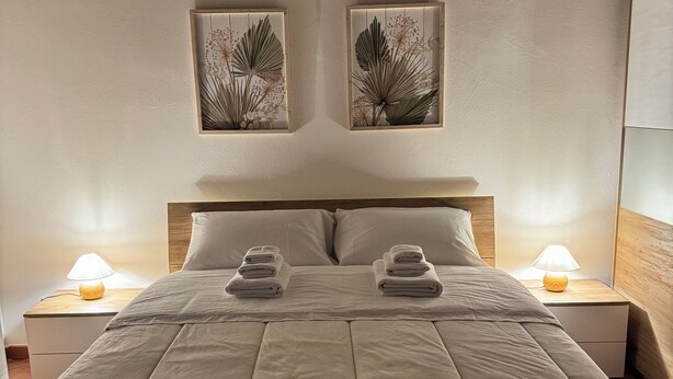 A neatly made bed with a headboard, two bedside tables with lamps, and two wall-mounted artwork pieces. - The sweet little house (Palermo)