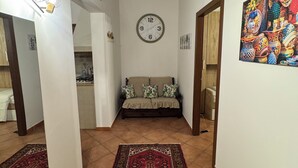 A hallway with a patterned rug, a sofa with cushions, a wall clock, and a colorful painting. - The sweet little house (Palermo)