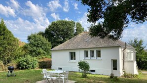 Une maison blanche avec un toit en tuiles, un petit porche et un coin repas comprenant une table et des chaises.