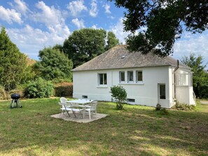 Een wit huis met een pannendak, een klein terras en een eethoek met een tafel en stoelen.