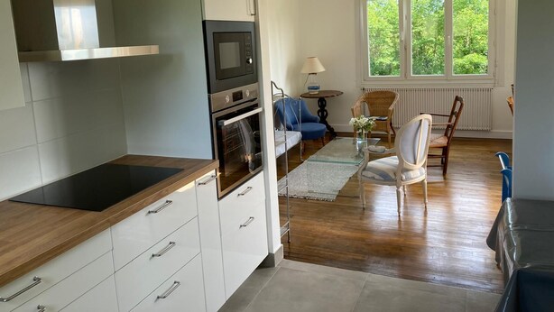 Une cuisine moderne dotée d’un four à micro-ondes et d’un four encastrés, un coin repas avec une table et des chaises, et une grande fenêtre donnant sur un paysage verdoyant.