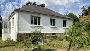 Une maison à deux étages, avec une façade blanche, des fondations en pierre et un petit porche à l’avant.