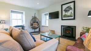 Ein gemütliches Wohnzimmer mit Sofa, Hängekorbschaukel, Kamin und Wandfernseher.