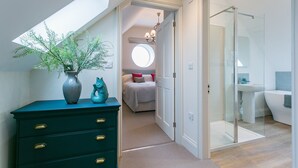 Ein modernes Schlafzimmer mit Dachfenster, einem Bett mit roten Kissen, einem Badezimmer mit Duschkabine und einer grünen Kommode mit Schubladen.