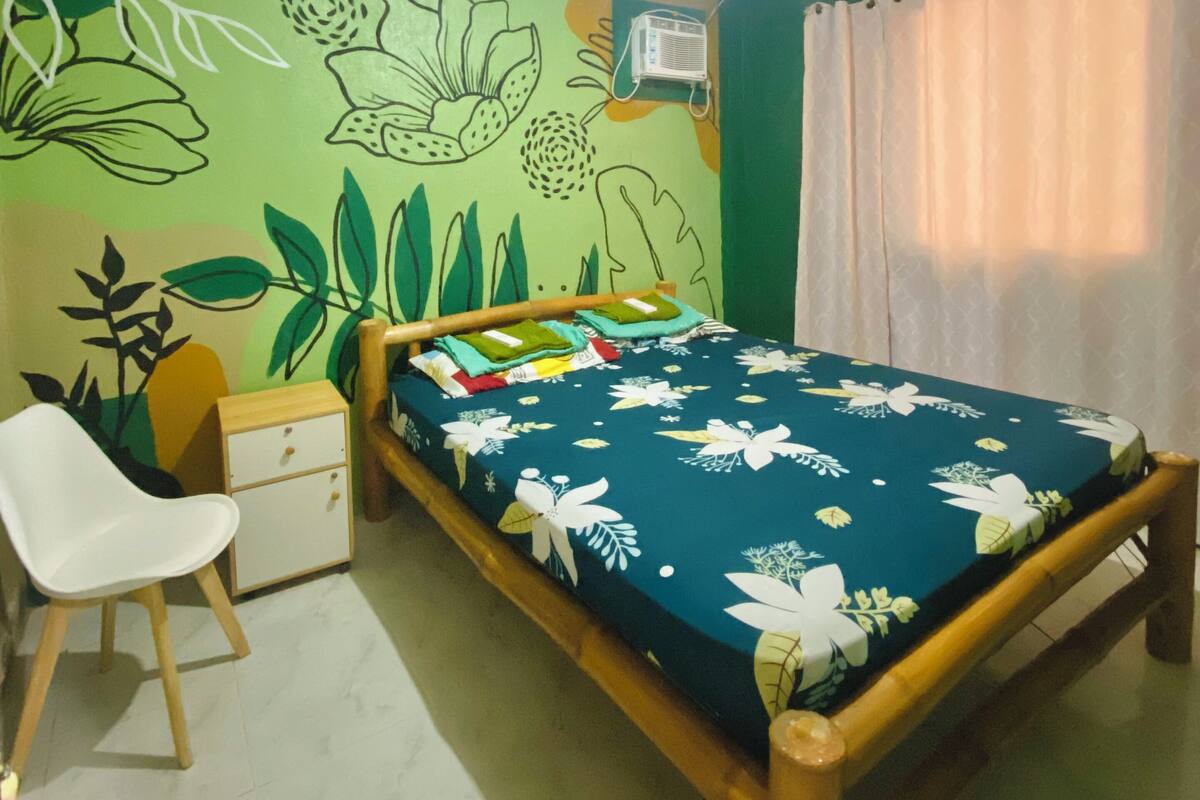Ein Schlafzimmer mit Bett, Stuhl, Nachttisch und einer Wand mit floralem Wandbild.