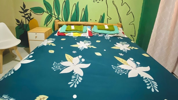 Een kamer met een bed, een nachtkastje, een stoel en een muur met een geel-groen muurschildering.