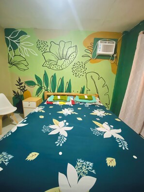 A room with a bed, a nightstand, a chair, and a wall with a green and yellow mural.