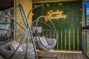 Uma cadeira suspensa com almofadas, uma placa de neon com a inscrição 'Smoky Mountains' e uma parede coberta por folhagem verde.