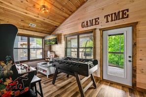 Un interior de madera con una mesa de fútbol de mesa, un televisor y una puerta que dice 'GAME TIME'.