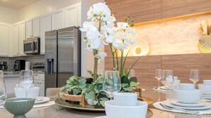 Een moderne keuken met roestvrijstalen apparatuur, een eettafel gedekt met witte serviesgoed en glazen, en een decoratieve orchidee als middelpunt.