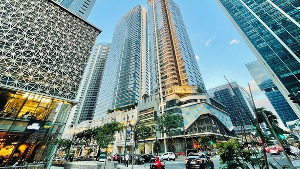 A cityscape with tall modern buildings, a prominent glass structure, and a busy street with cars and pedestrians. - Uptown Parksuites 2 (Taguig)