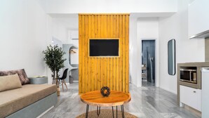 Ein modernes Wohnzimmer mit einer Wand in Holzoptik, einem runden Holztisch, einer Couch und einem an der Wand befestigten Fernseher.