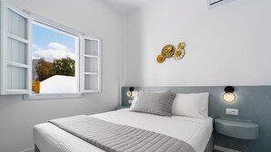Ein Schlafzimmer mit Bett, Nachttisch, Wandleuchten und einem Fenster mit Blick auf Bäume.
