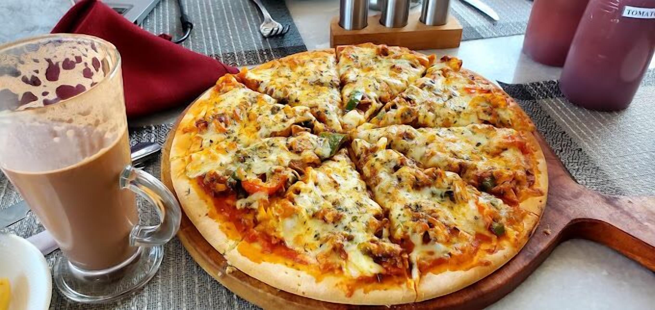 Una pizza sobre una tabla de madera, con un vaso de una bebida marrón a su lado.