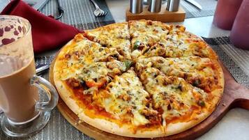 Una pizza sobre una tabla de madera, con un vaso de una bebida marrón a su lado.