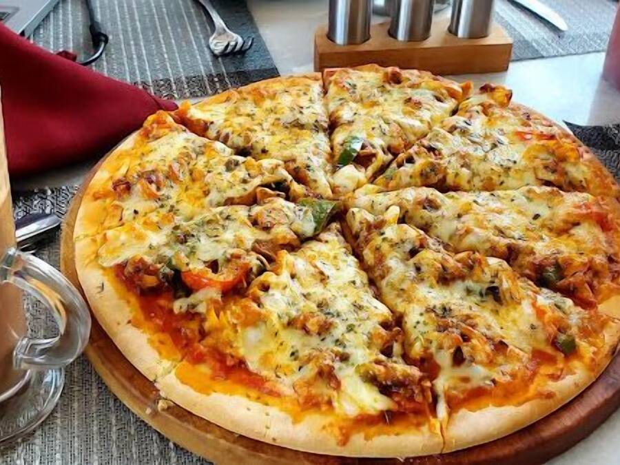 Una pizza sobre una tabla de madera, con un vaso de una bebida marrón a su lado.