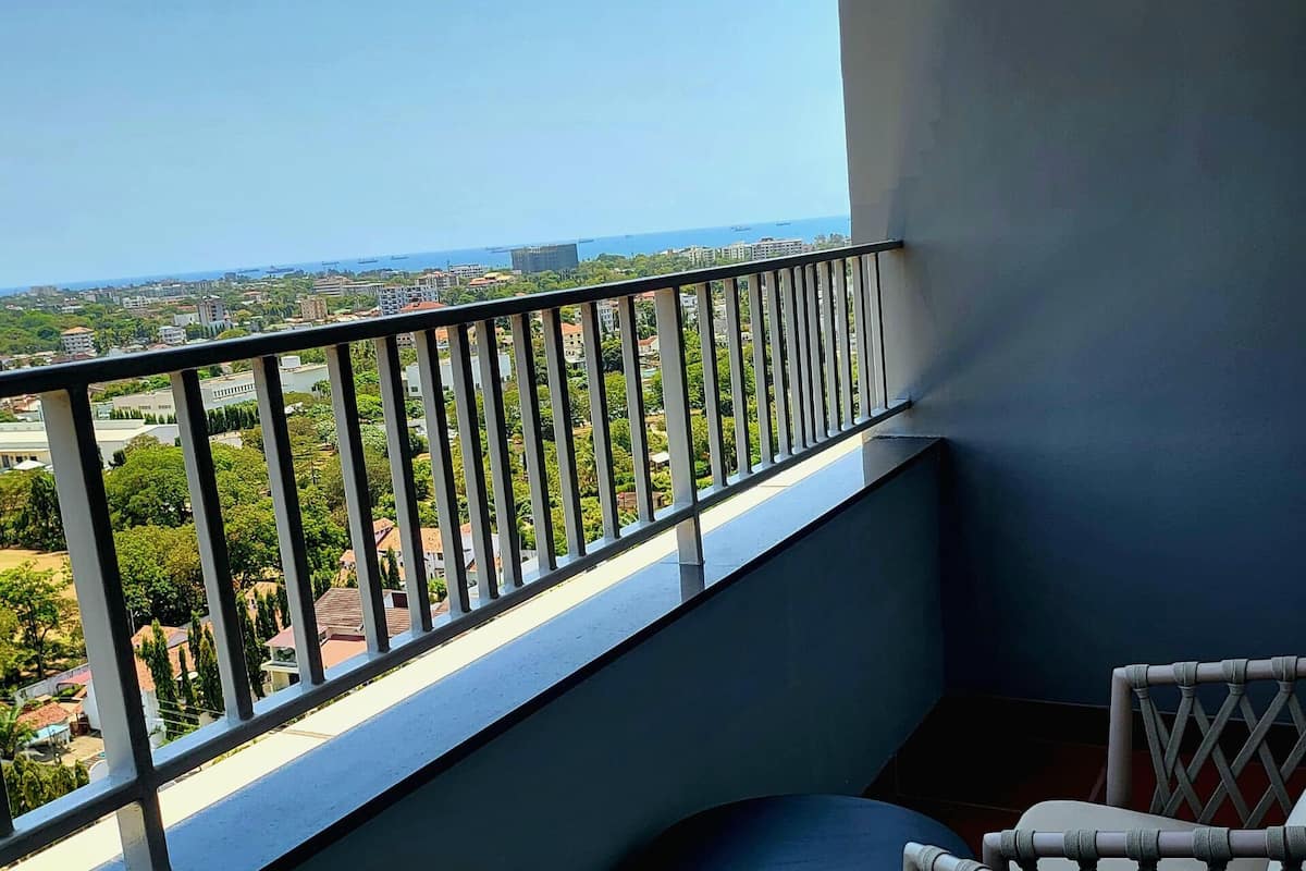 Ein Balkon mit Blick auf eine Stadtlandschaft und das Meer. Zwei Korbstühle mit Kissen sind vorhanden.