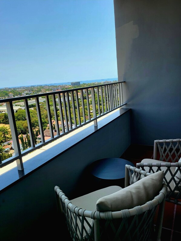Un balcon avec vue sur le paysage urbain et la mer. On y trouve deux fauteuils en osier avec des coussins.