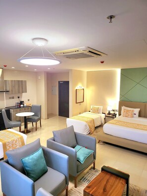 Une chambre d’hôtel comprenant un coin repas, deux lits, un bureau et un espace salon avec des fauteuils et une table basse.