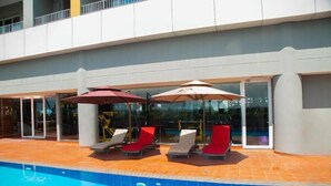 A swimming pool with sun loungers and umbrellas, surrounded by a building with large glass doors. - Kingjada Hotel  (Dar es Salaam)
